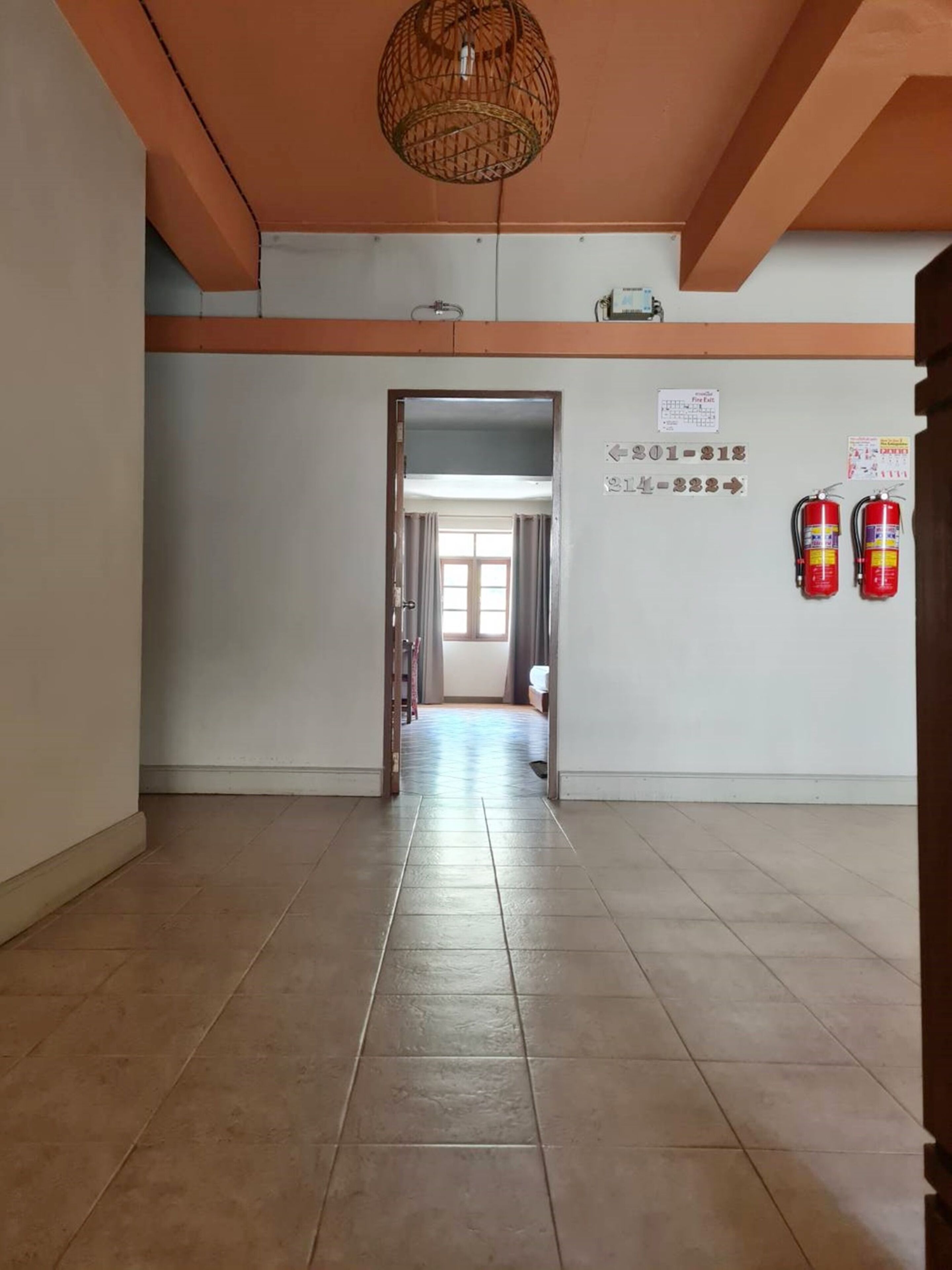 A hallway with a tiled floor, a door leading to another room, and fire extinguishers on the wall.