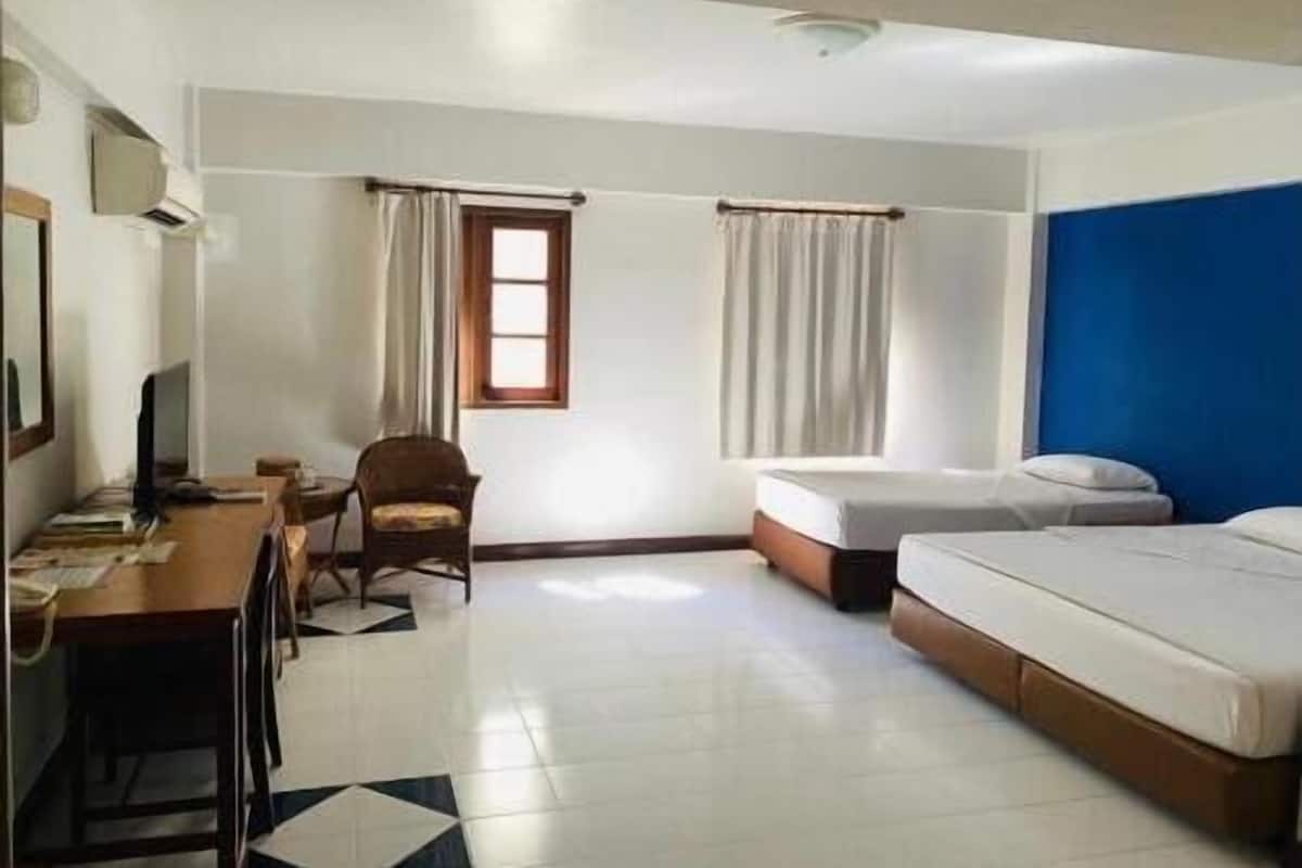 A hotel room with a bed, a desk, a chair, and two windows with curtains.