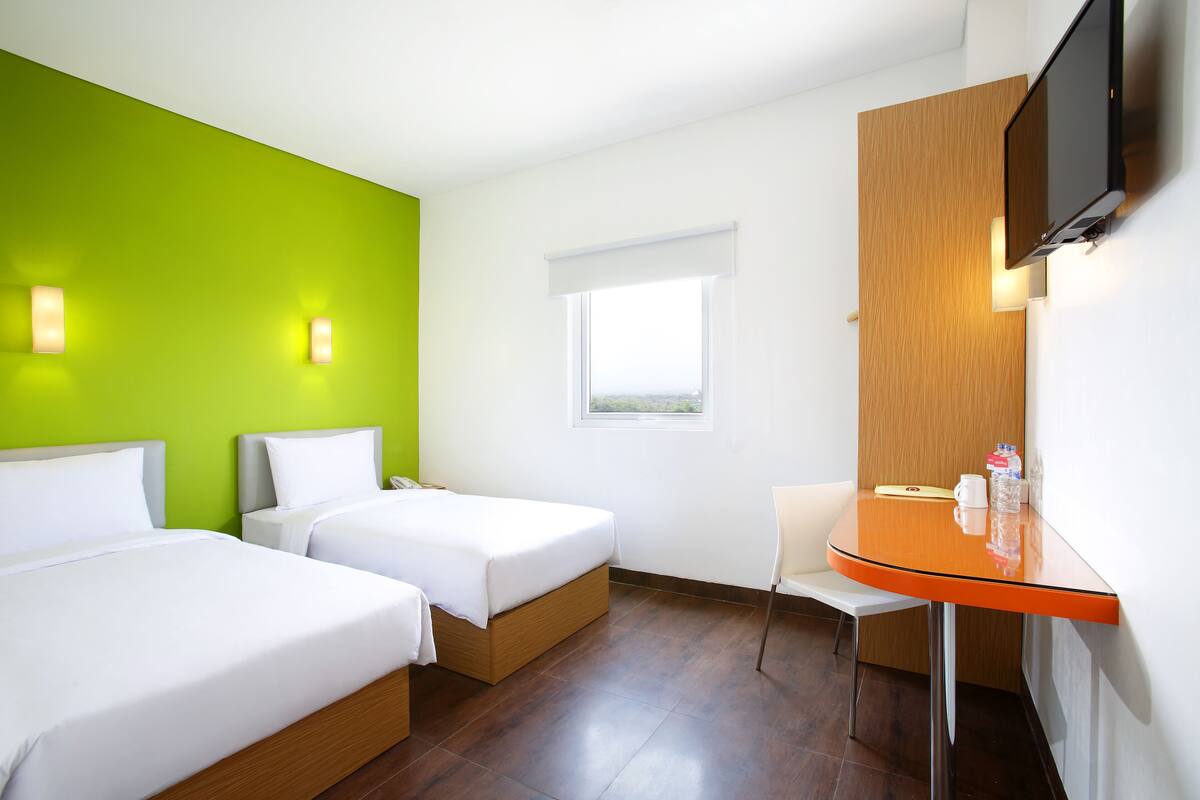A hotel room with two beds, a small table, a chair, a TV, and a window.