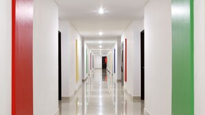 A long, well-lit hallway with white walls and doors in various colors.