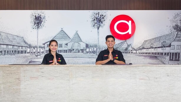 Two individuals at a reception desk with a mural of traditional buildings in the background.