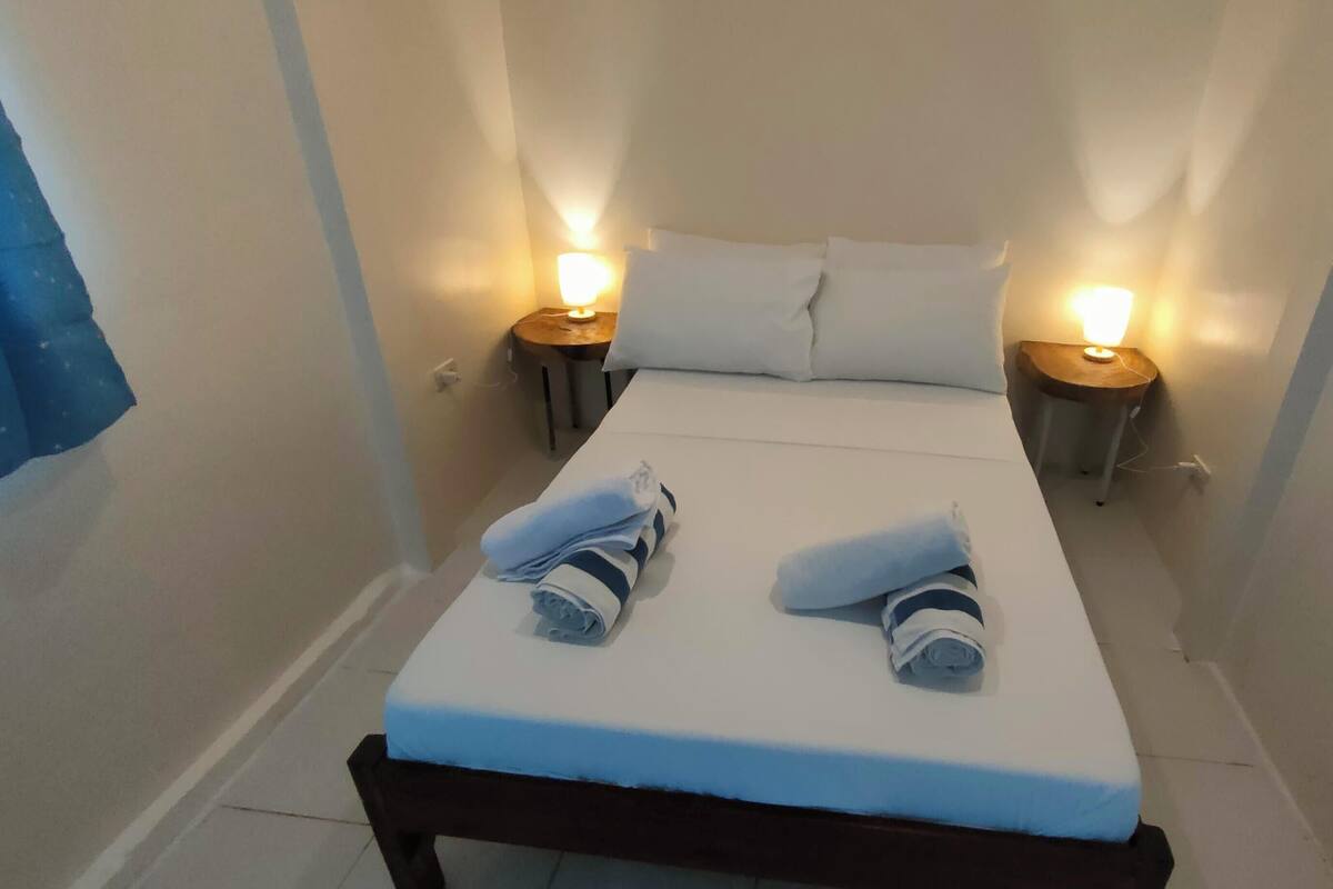A small, narrow hotel room with a single bed, two bedside tables with lamps, and a window with curtains.