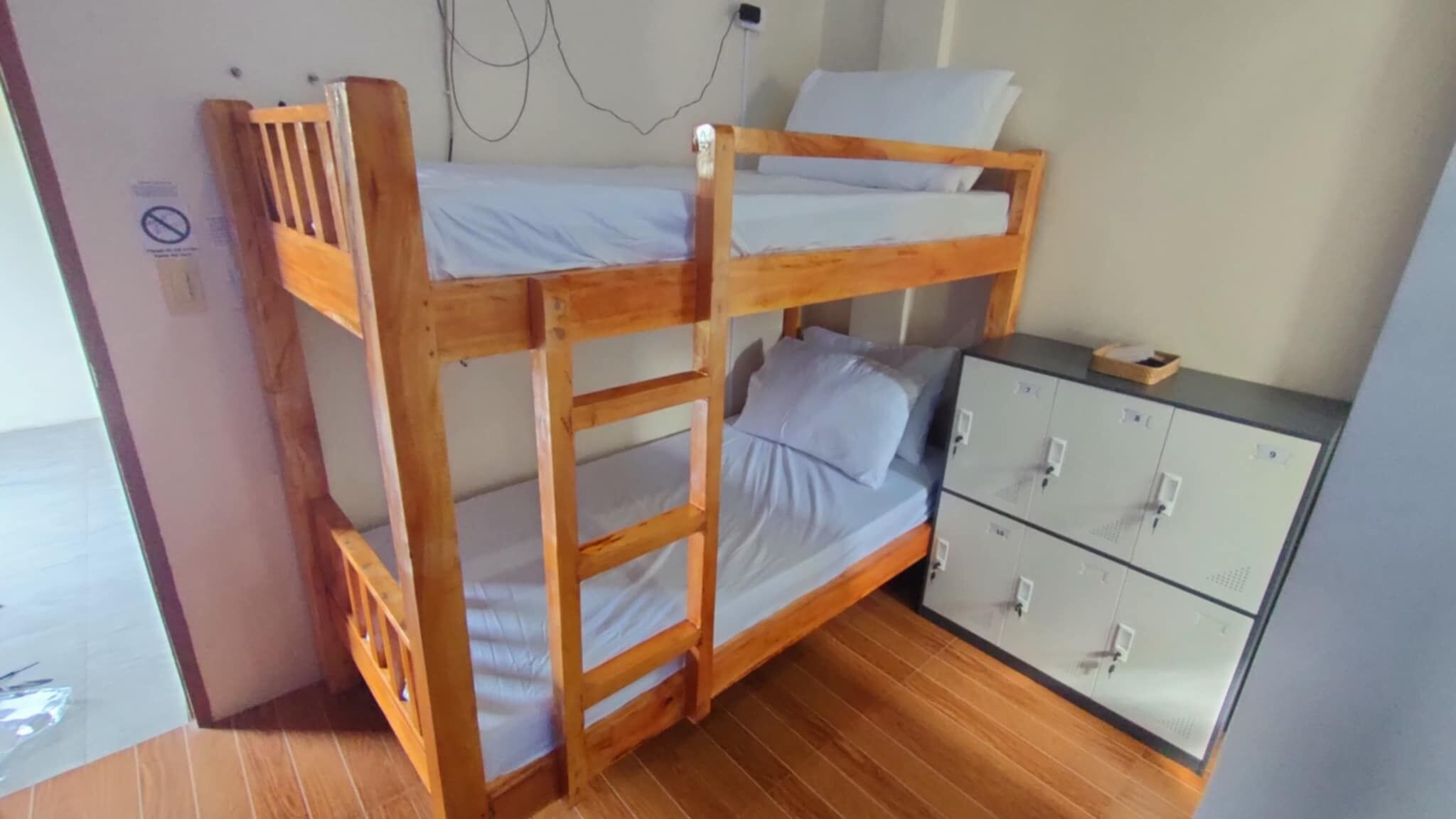 A bunk bed with a wooden frame, a small desk with drawers, and a wall socket.