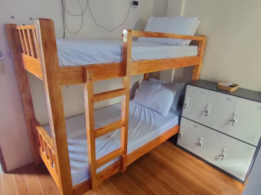 A bunk bed with a wooden frame, a small desk with drawers, and a wall socket.