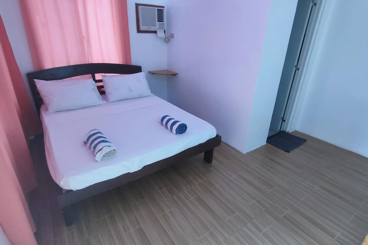 A single bed with white bedding and striped towels, a bedside table, and a wall-mounted air conditioner.