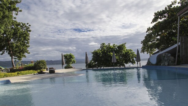 A large outdoor swimming pool with a view of the water, surrounded by trees and a wooden deck. - Isla Hayahay Beach Resort and Restaurant (Calape)