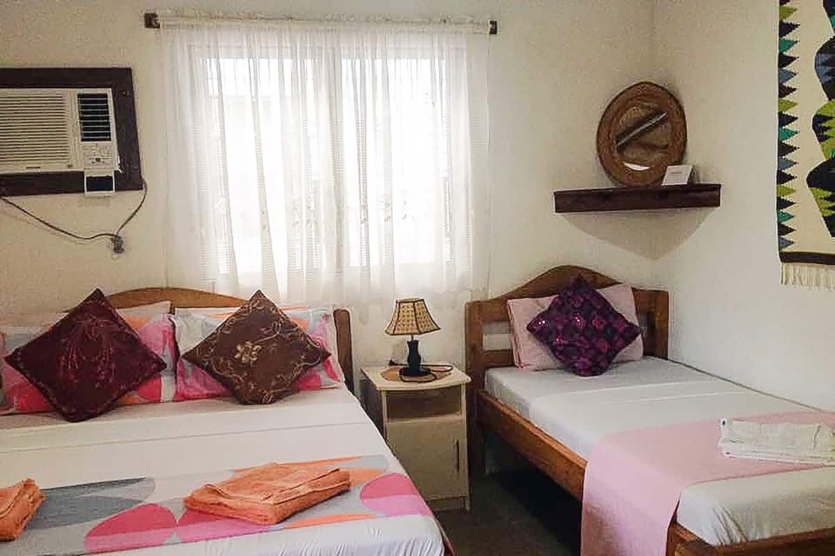 A room with two beds, a nightstand with a lamp, a wall-mounted air conditioner, and a decorative mirror.