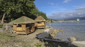 Two thatched-roof huts by a calm lake, wooden deck, and a distant pier. - Isla Hayahay Beach Resort and Restaurant (Calape)