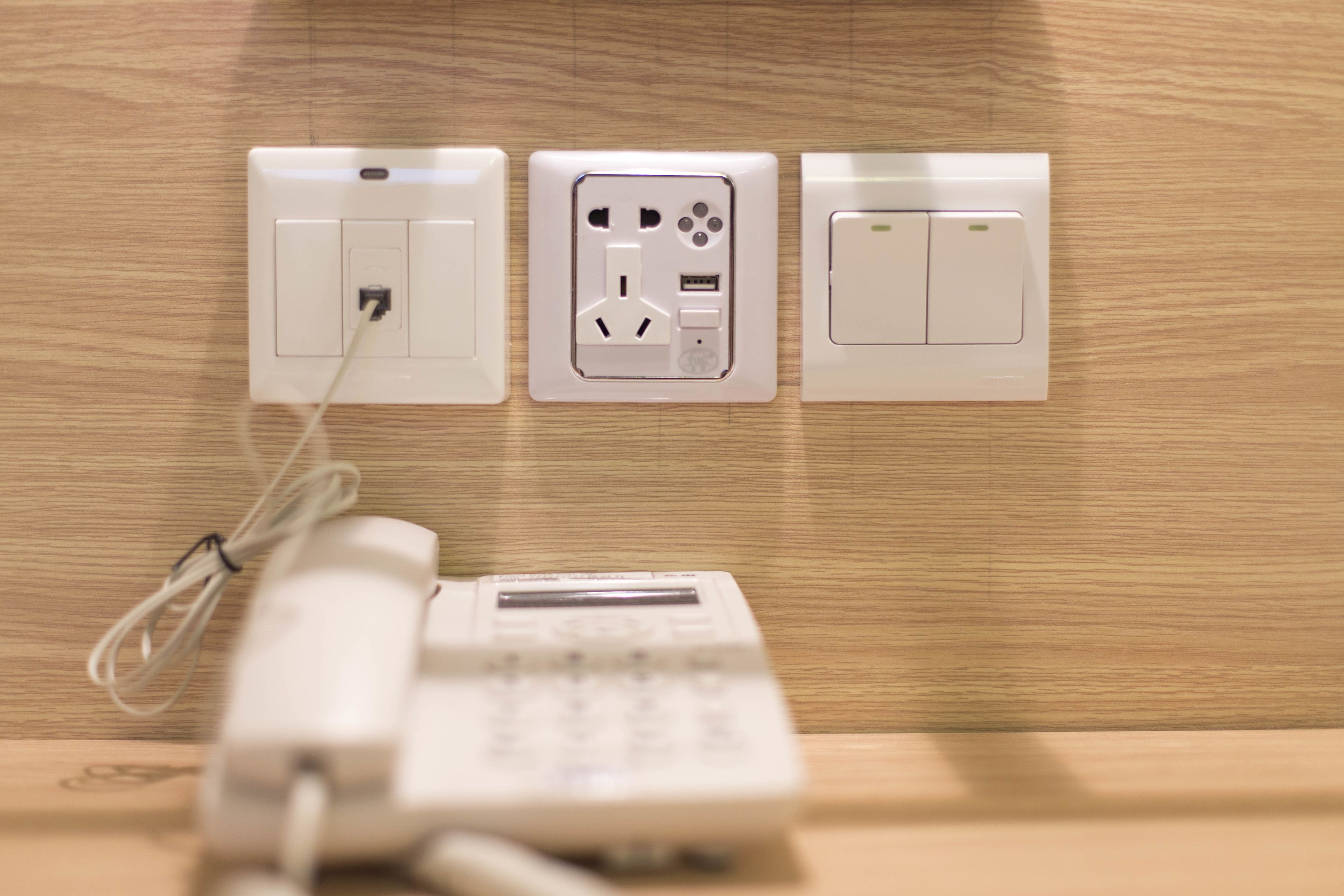 A wall-mounted electrical outlet with a phone and charger plugged in.