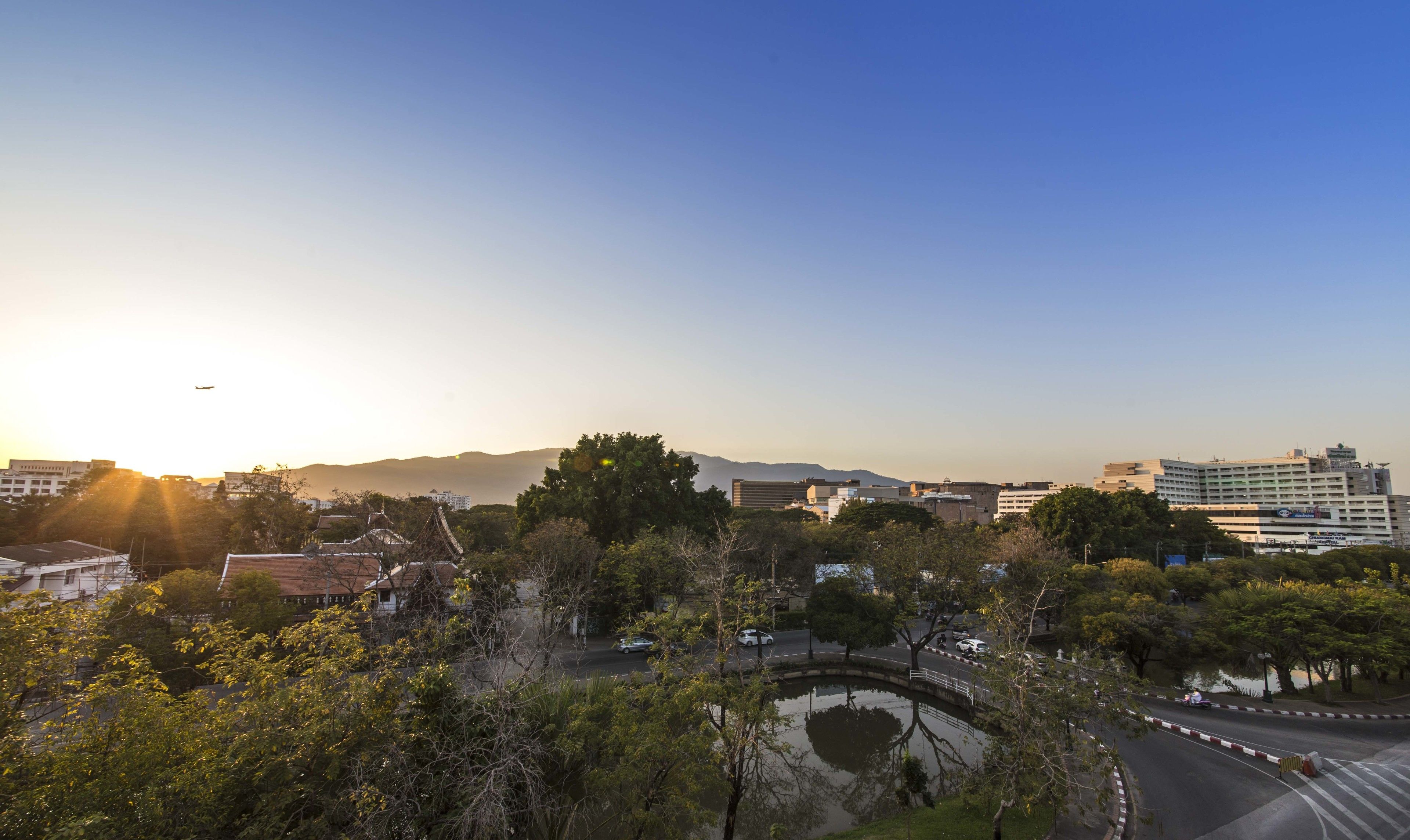 A cityscape with a mix of modern and traditional architecture, a curved road, and a body of water reflecting the surroundings.