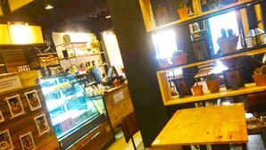 A cozy cafe with wooden furniture and a display case filled with pastries. - Chiang Roi 7 Days Inn (Chiang Mai)