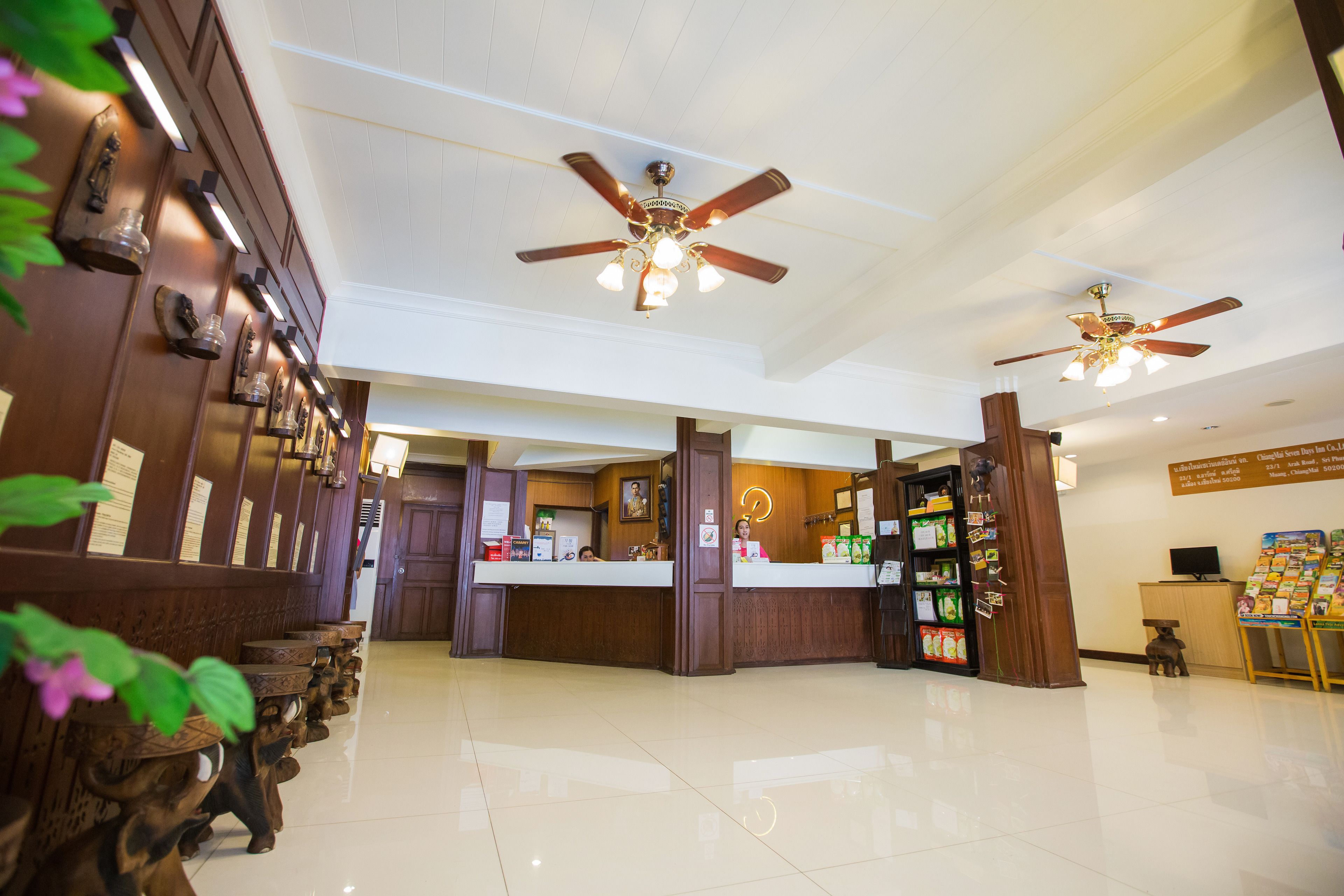 A hotel lobby with wooden reception desks, ceiling fans, and a clean, tiled floor.