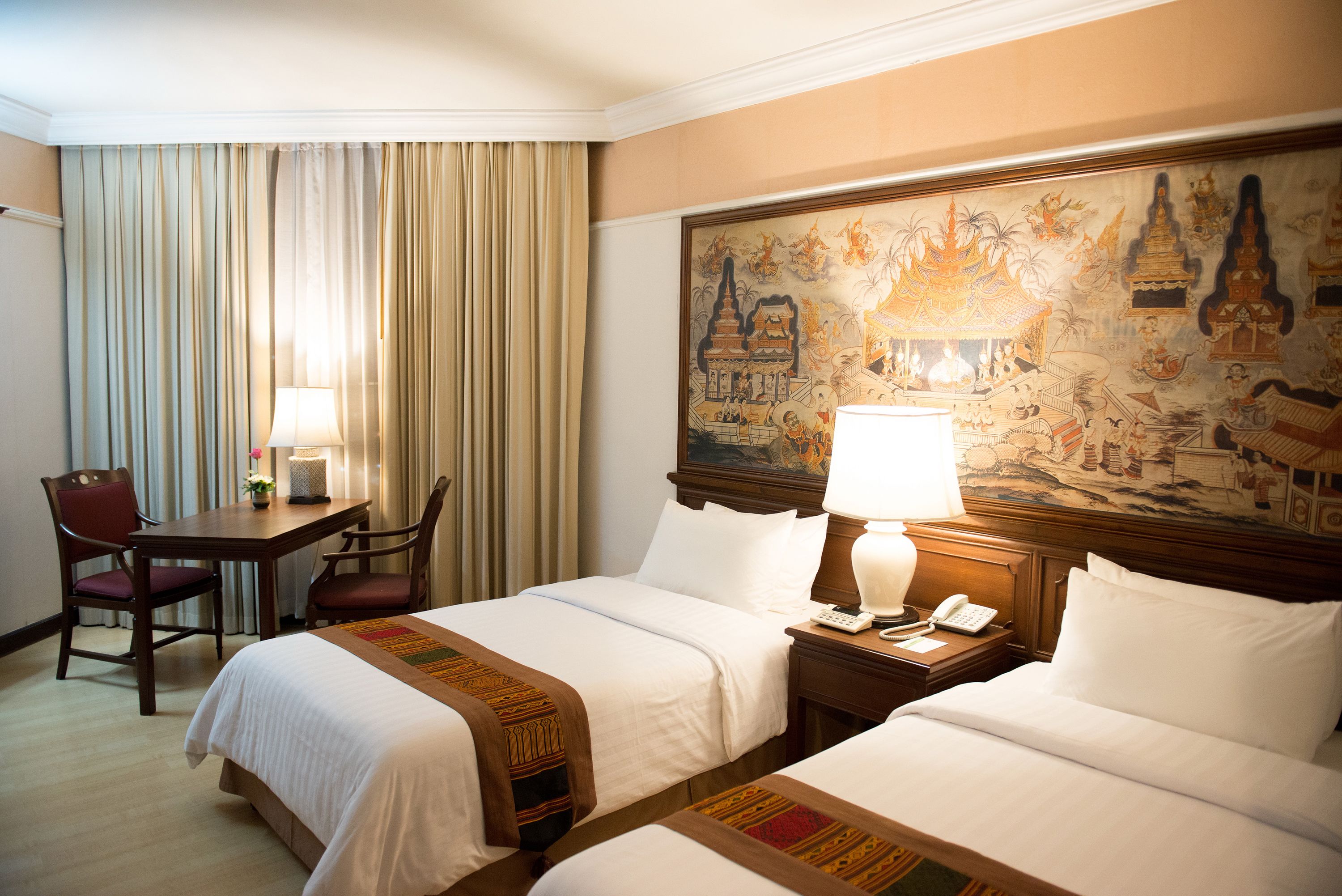 Une chambre d’hôtel avec deux lits, un bureau avec une chaise, une lampe et un tableau au mur.