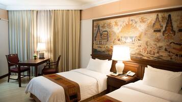 Une chambre d’hôtel avec deux lits, un bureau avec une chaise, une lampe et un tableau au mur.