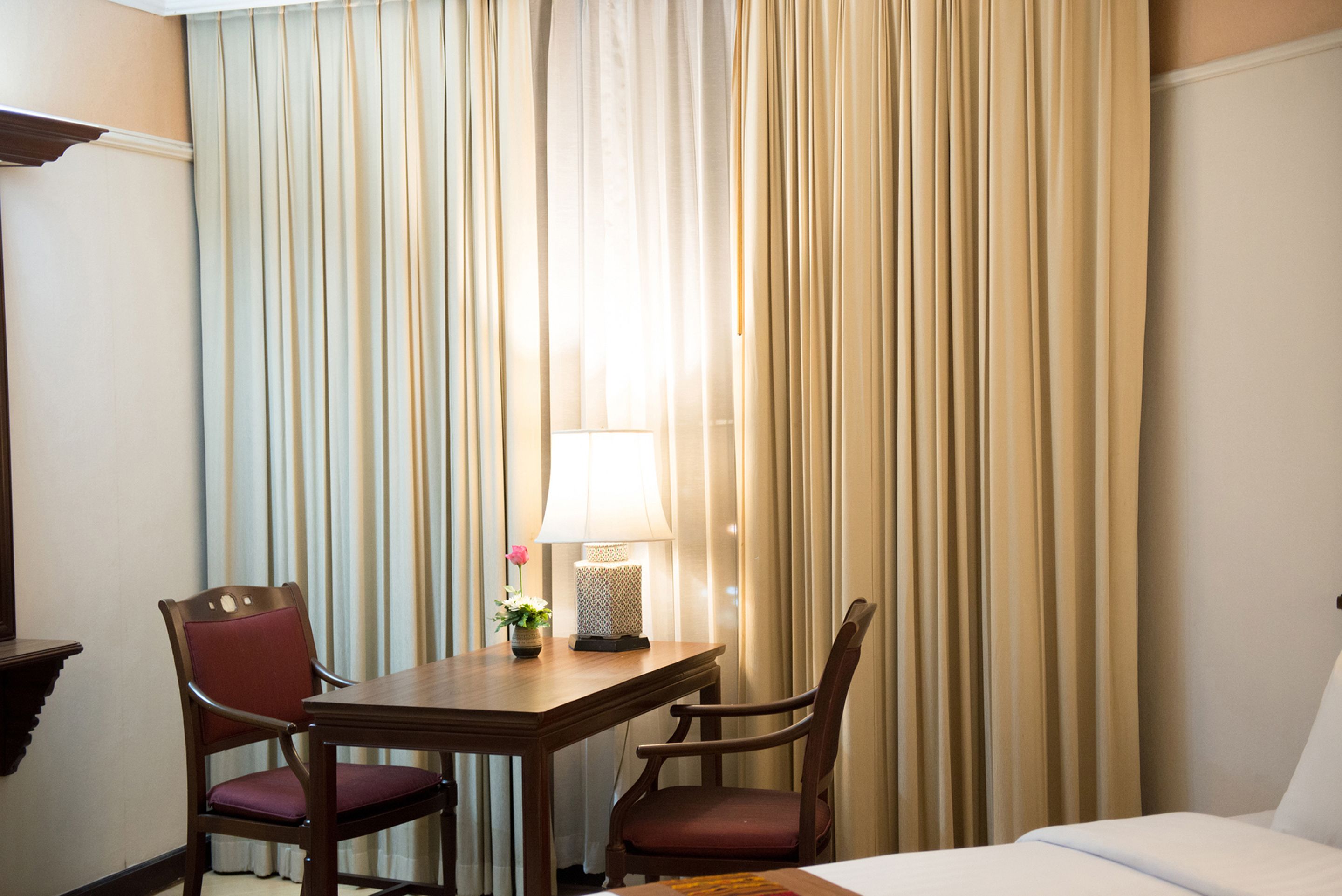 Une chambre d’hôtel avec un bureau en bois, deux chaises, une lampe et un lit.