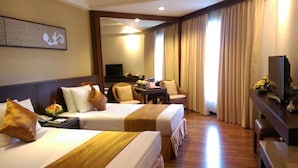 A hotel room with two beds, a desk, a television, and a dining area.