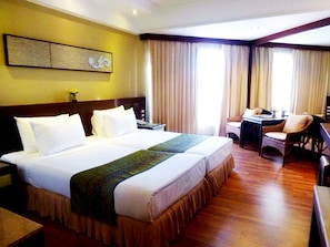 A hotel room with a large bed, a desk, two chairs, and a view of the outdoors through the window.