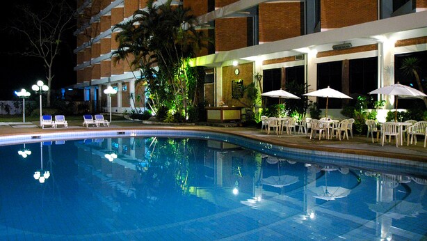 A swimming pool with lounge chairs and umbrellas, surrounded by a building with brick walls and large windows.