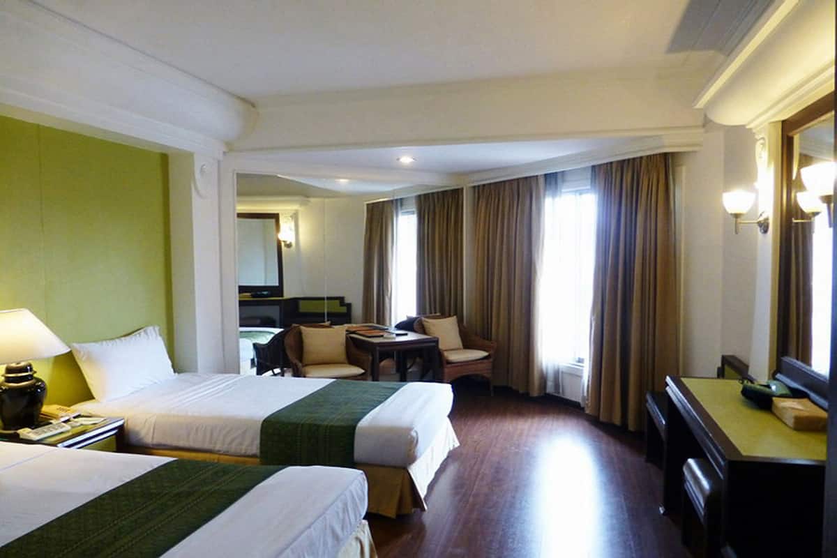 A hotel room with two beds, a desk, a chair, a small table, and a mirror.