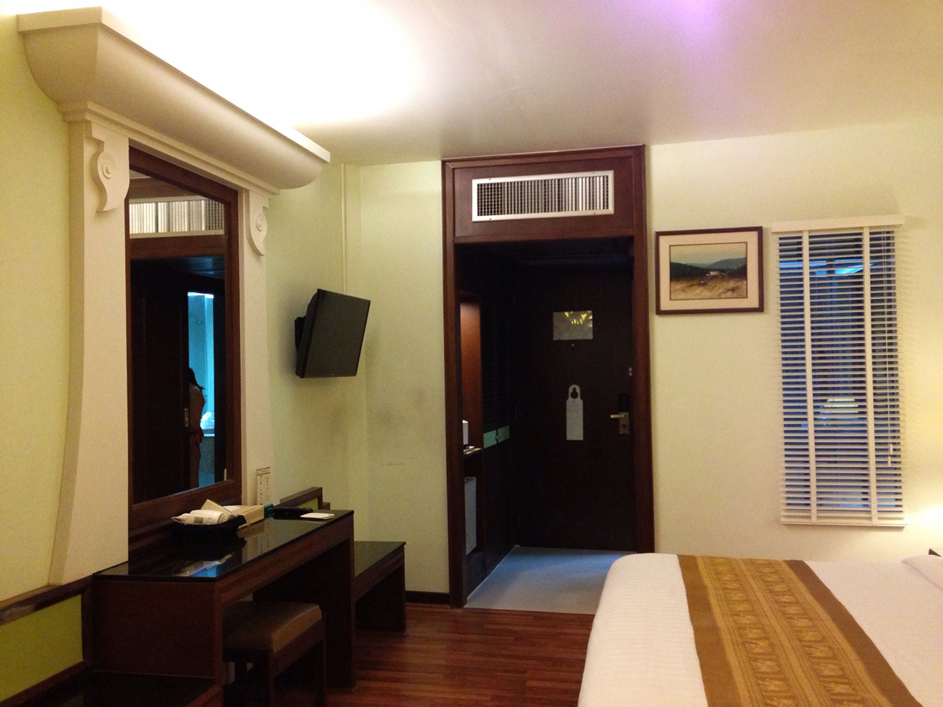Une chambre d’hôtel équipée d’un lit, d’un bureau, d’une chaise, d’une télévision, d’une porte et d’une fenêtre avec des stores.
