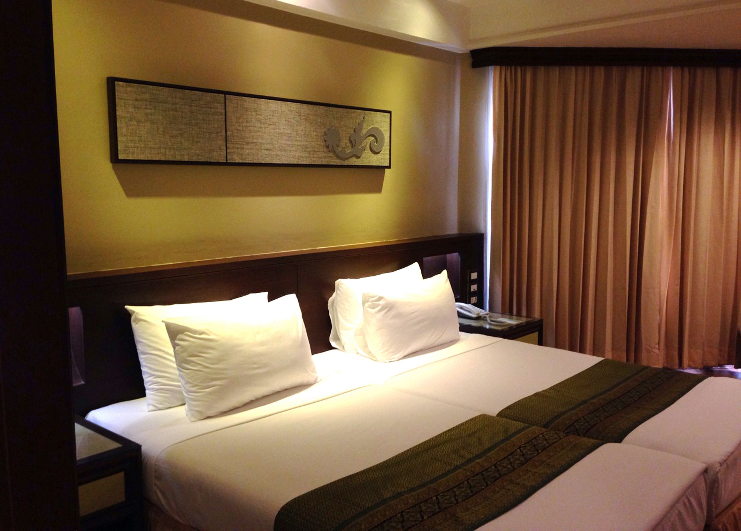 A hotel room with a large bed, two pillows, a bedside table with a phone, and a wall-mounted artwork.
