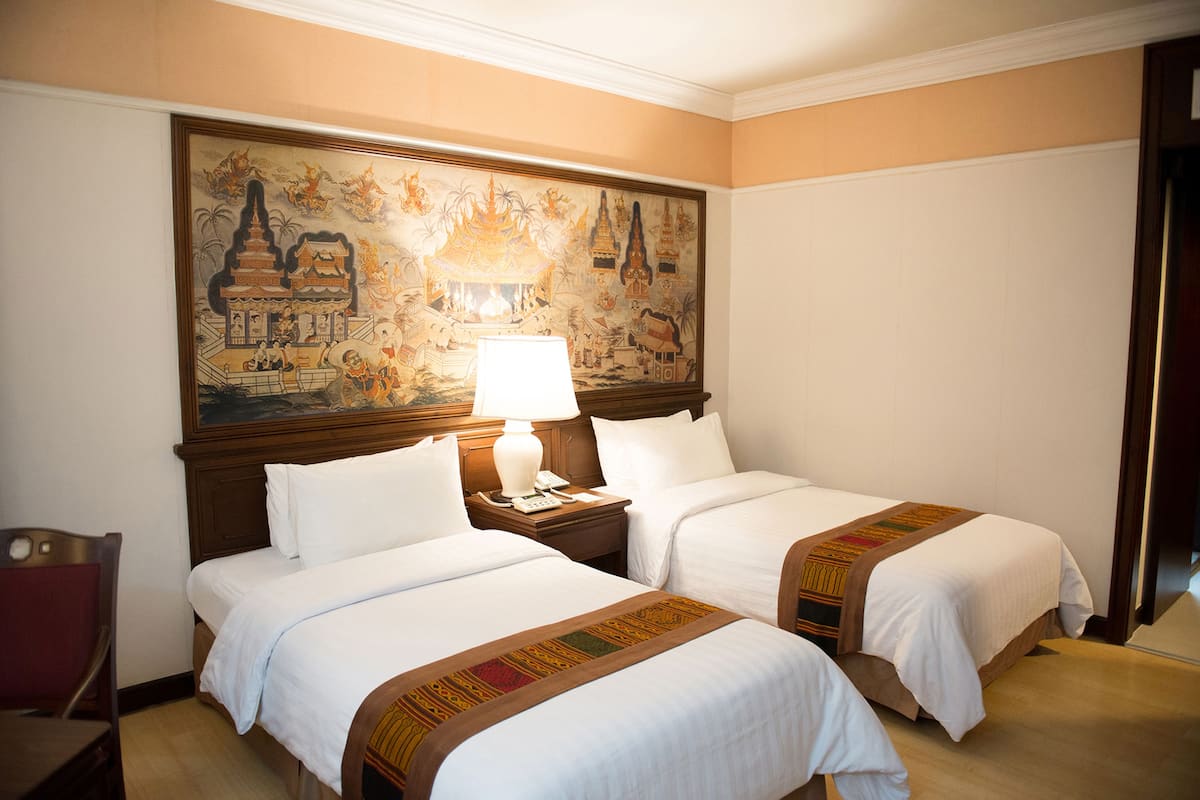 A hotel room with two beds, a nightstand with a lamp, and a large mural on the wall.