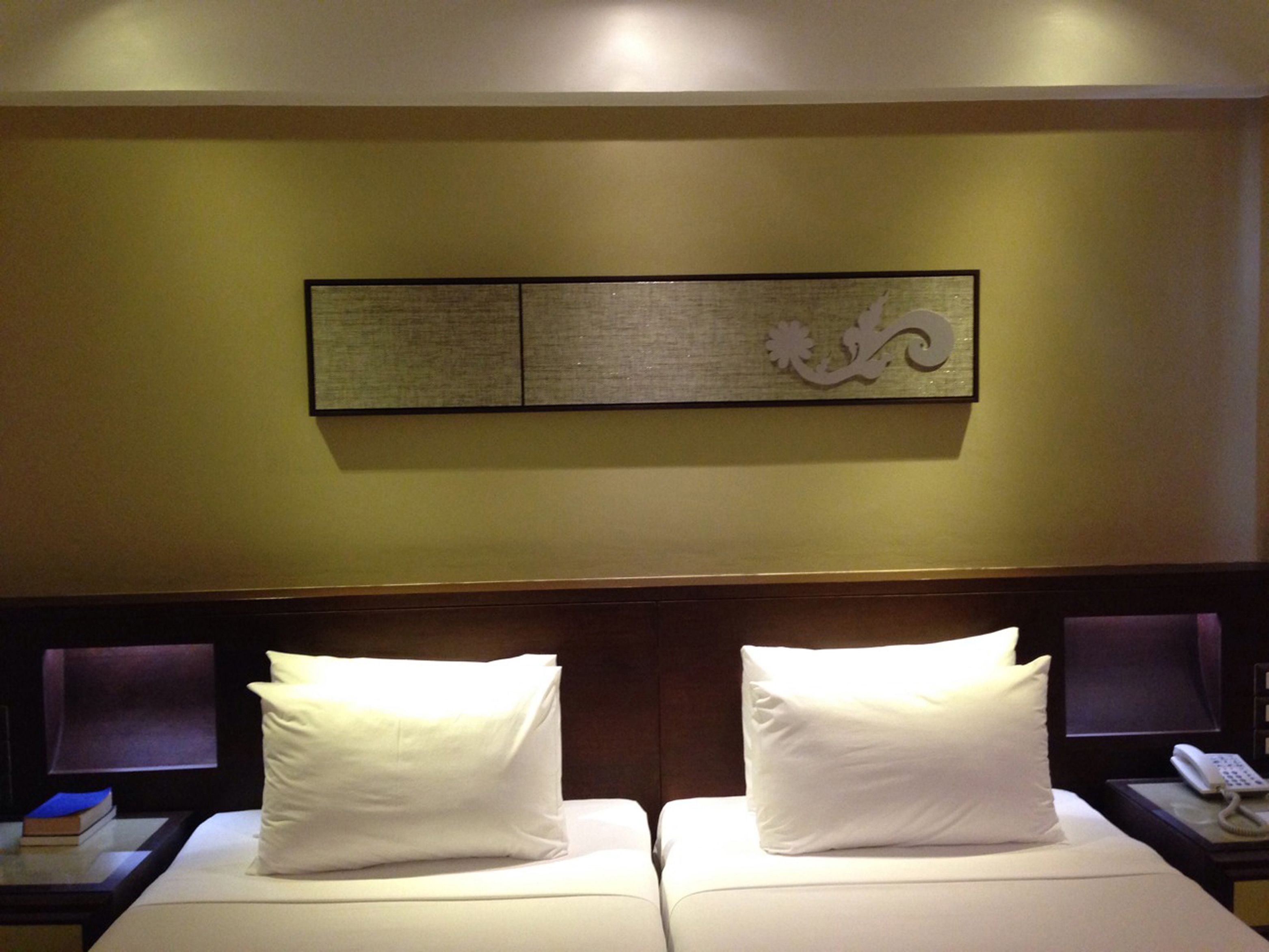 Una habitación de hotel con dos camas, una mesita de noche con teléfono y una obra de arte colgada en la pared.
