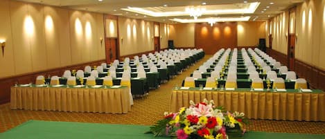 A conference room with rows of tables, each with a green tablecloth and white chairs, and a floral centerpiece on the front table.
