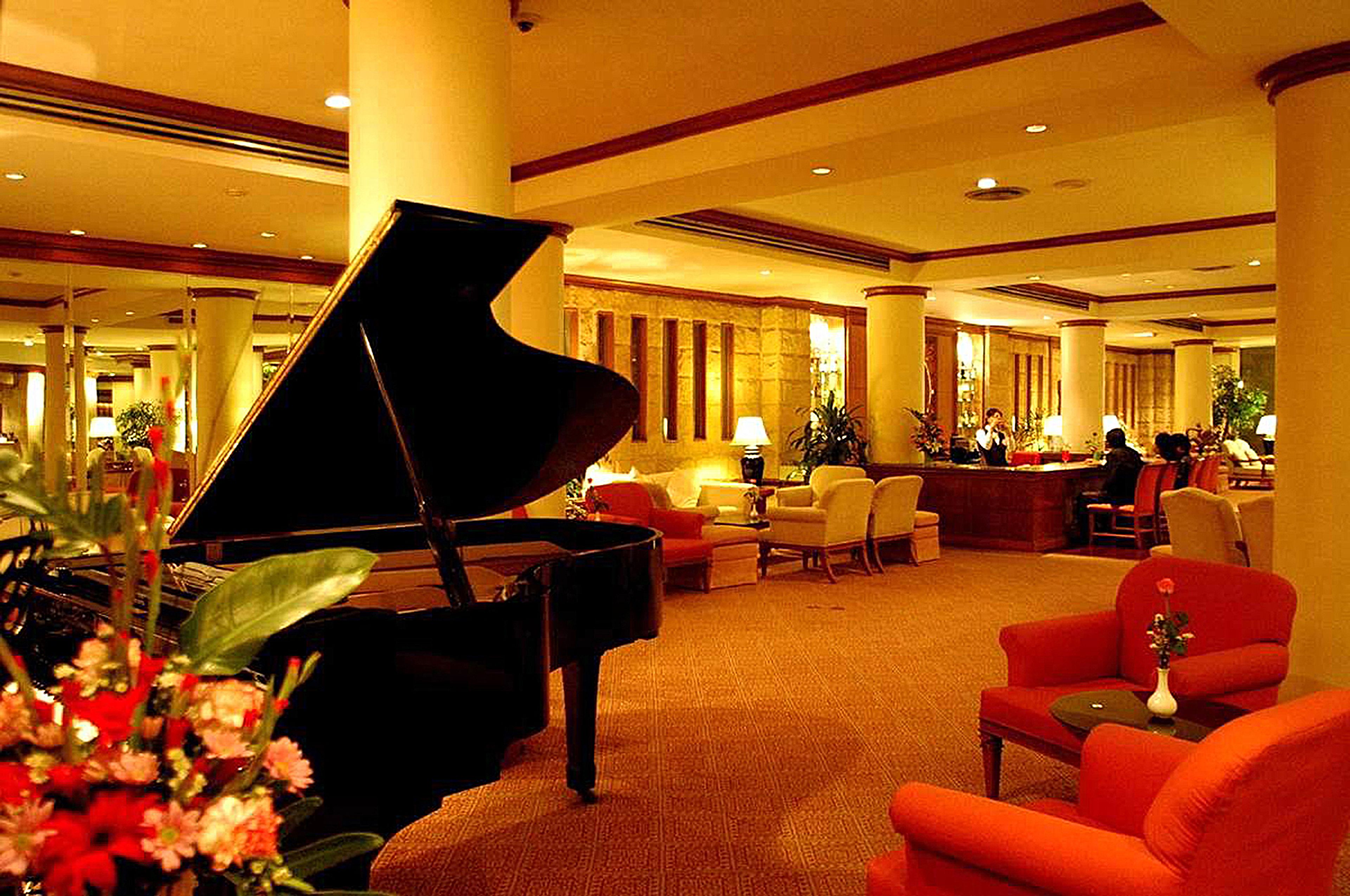 A grand piano in a spacious lobby with a reception desk, comfortable seating, and decorative plants.