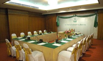 Uma sala de conferências com uma mesa comprida, cadeiras brancas com fitas douradas e um painel com um logotipo e texto.