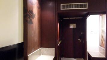 A hotel room with a wooden wall, a flat-screen TV, a small bedside table, and a window with blinds.