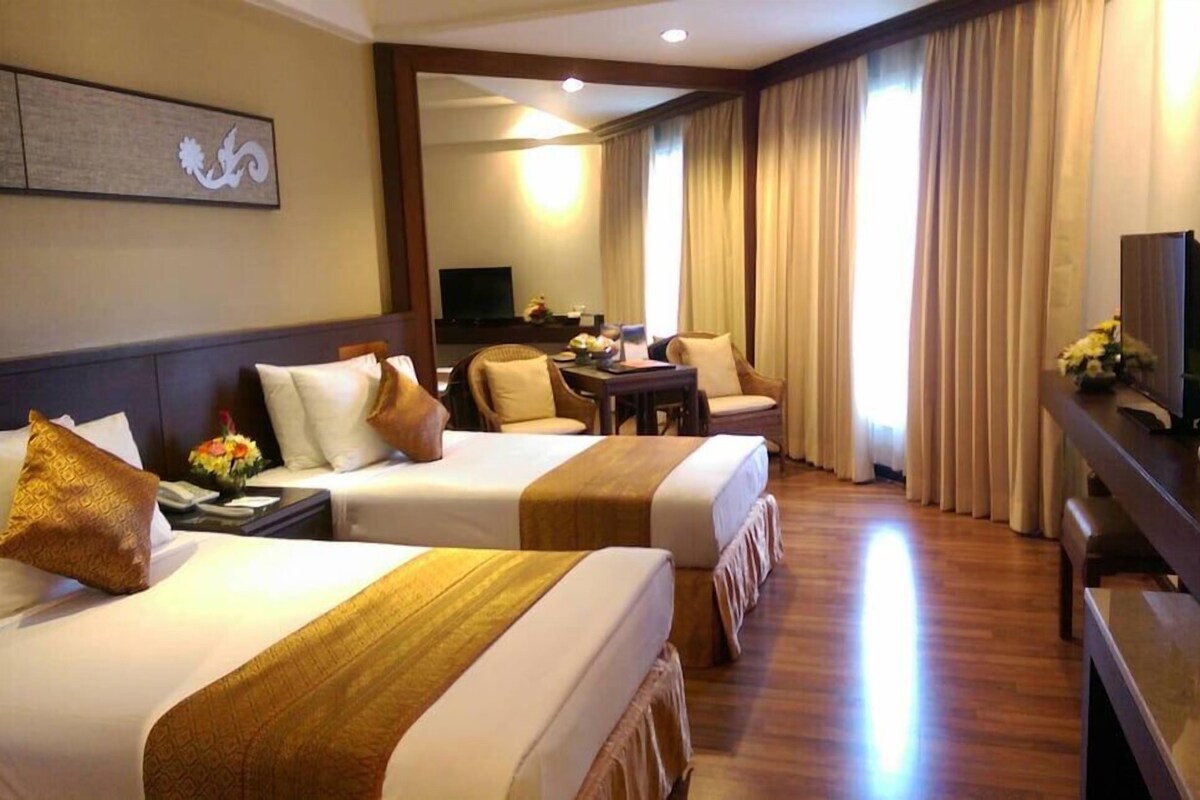 A hotel room with two beds, a desk, a TV, and a large window with curtains.