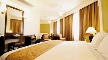 A hotel room with a large bed, a desk, a chair, a lamp, and a mirror.
