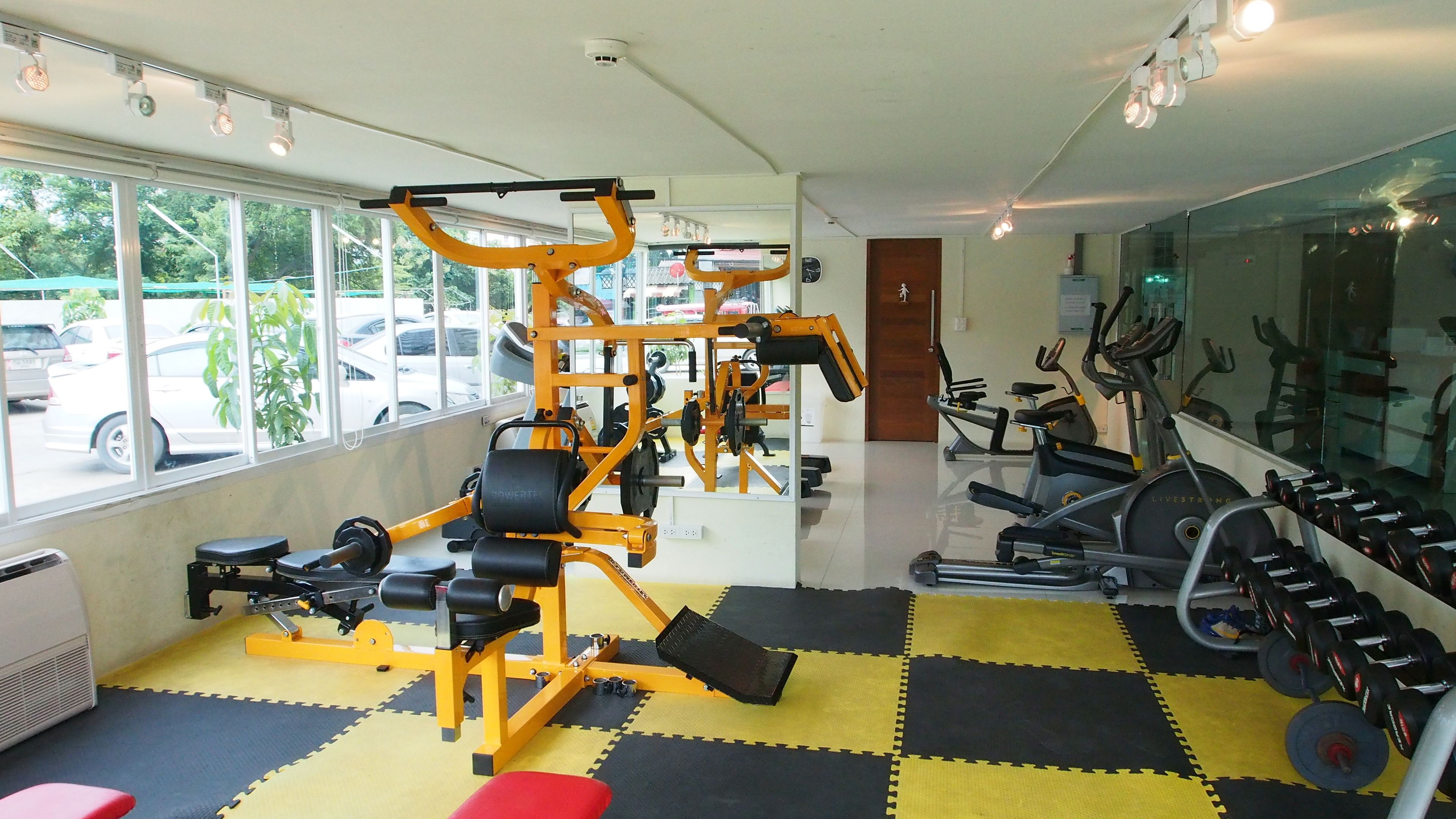 A gym with exercise equipment, a mirrored wall, and a view of parked cars outside.