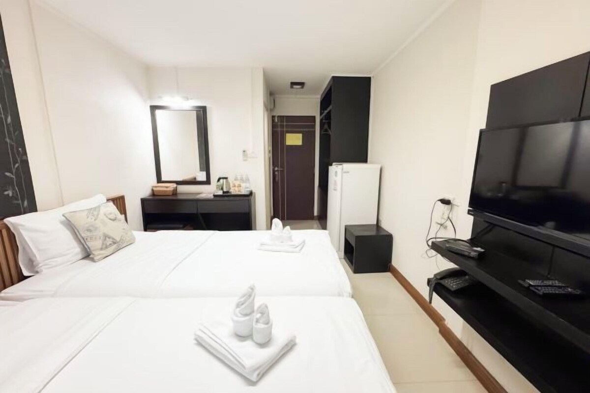 A hotel room with two beds, a TV, a desk with a mirror, and a wardrobe.