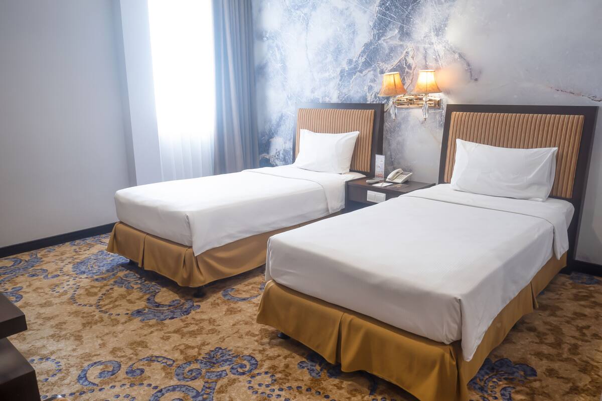 A hotel room with two beds, a patterned carpet, and a marble wall.