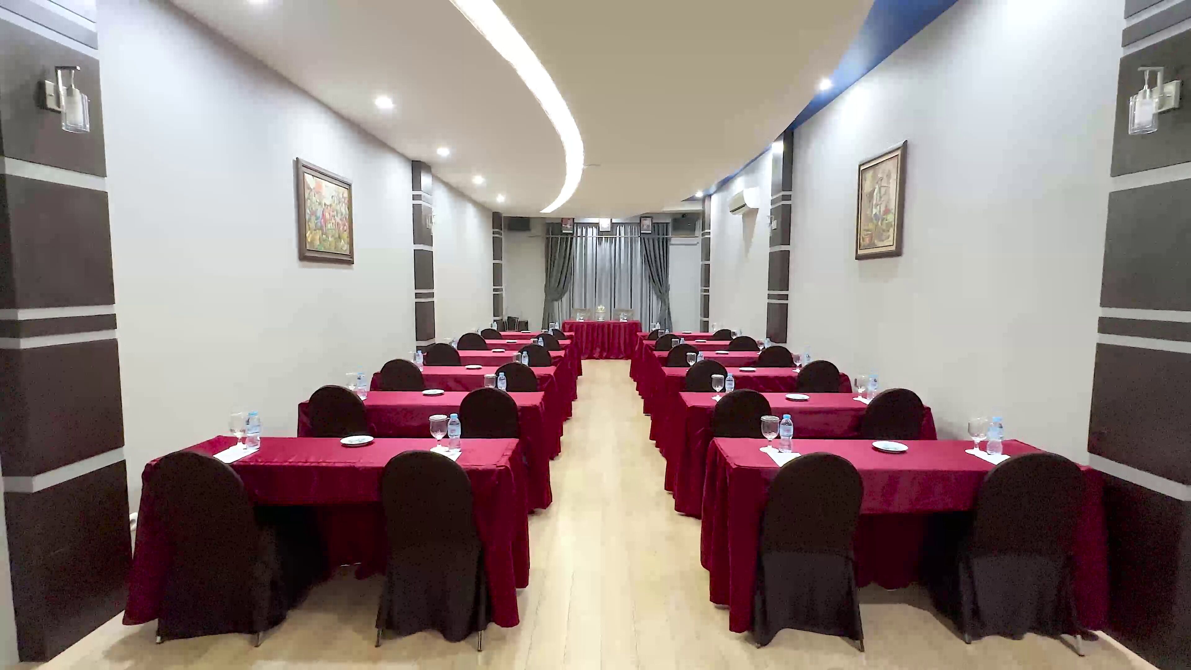 Un salón de conferencias con filas de mesas, cada una con sillas, botellas de agua y vasos.