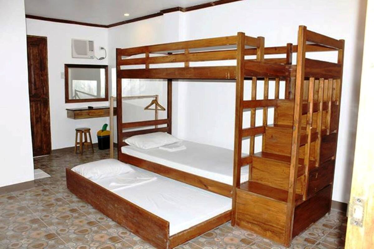 Habitación con literas de madera, un taburete pequeño, un espejo y un televisor.