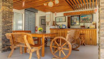 A rustic wooden interior with a wooden table and chairs, a vintage wooden cart, and a wooden counter with a menu board.