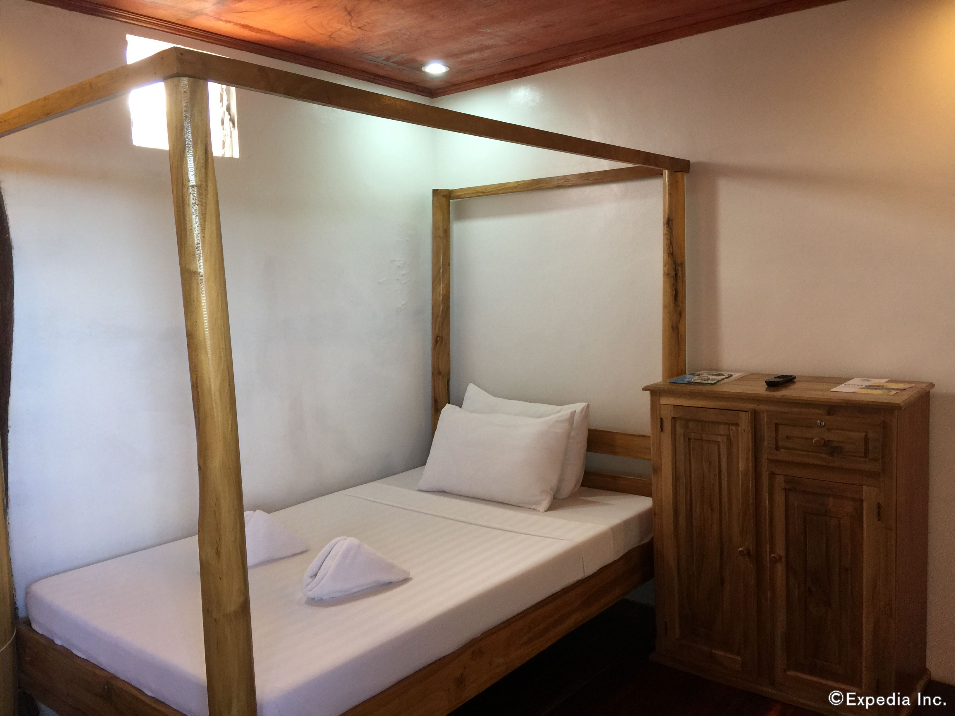 A single wooden bed with a canopy, a wooden nightstand with a drawer, and a small cabinet.