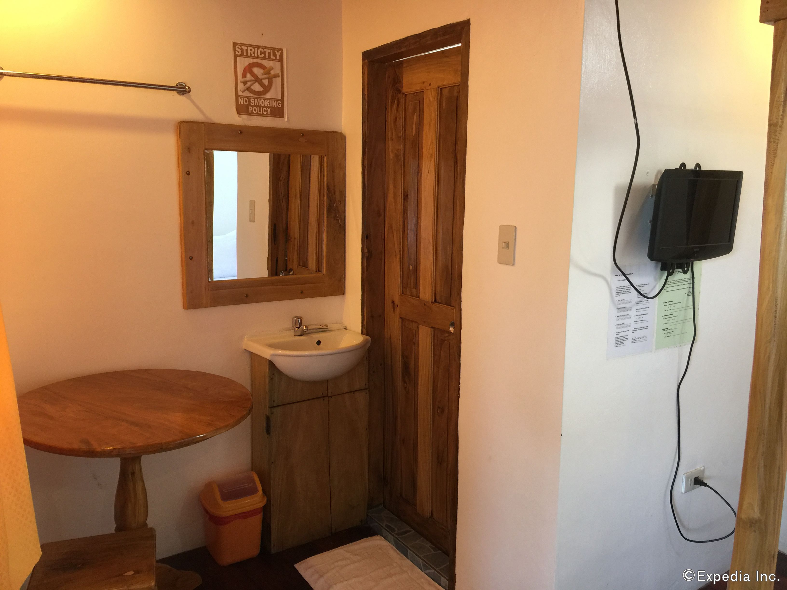 A bathroom with a wooden door, a sink, a mirror, a towel, and a trash bin.