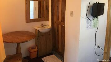 A bathroom with a wooden door, a sink, a mirror, a towel, and a trash bin.