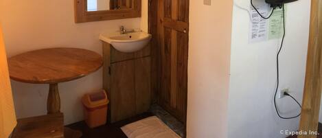 Un baño con puerta de madera, un lavamanos, un espejo, una toalla y un cubo de basura.