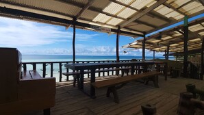 Una terraza de madera con mesas de picnic con vista a la playa.