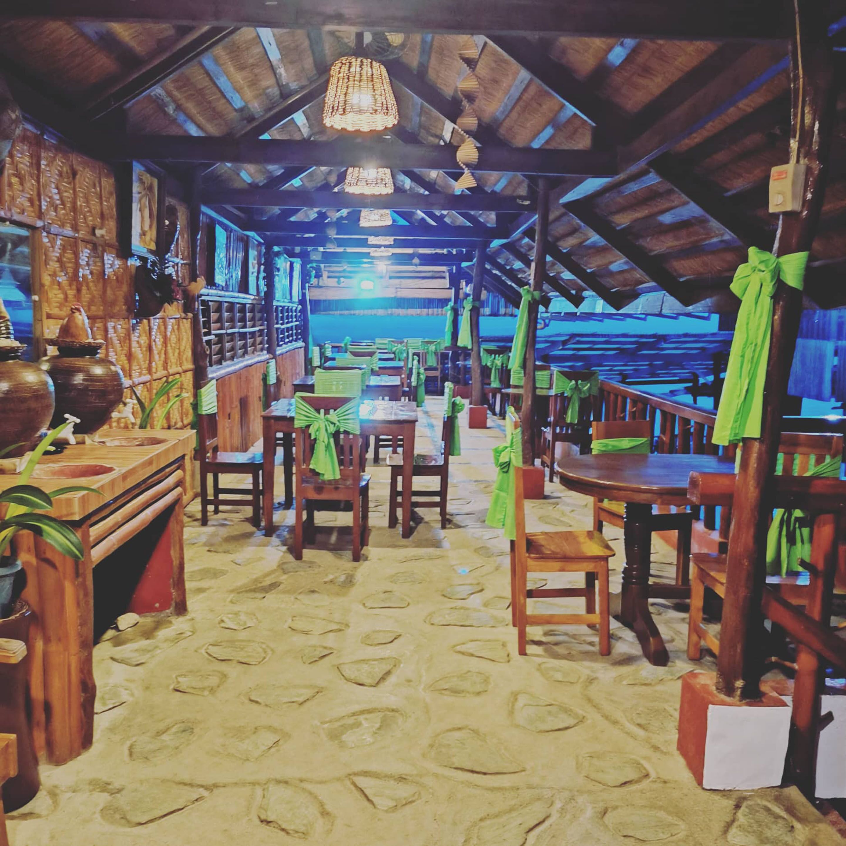 A rustic wooden interior with tables and chairs, a patterned floor, and a hanging light fixture.