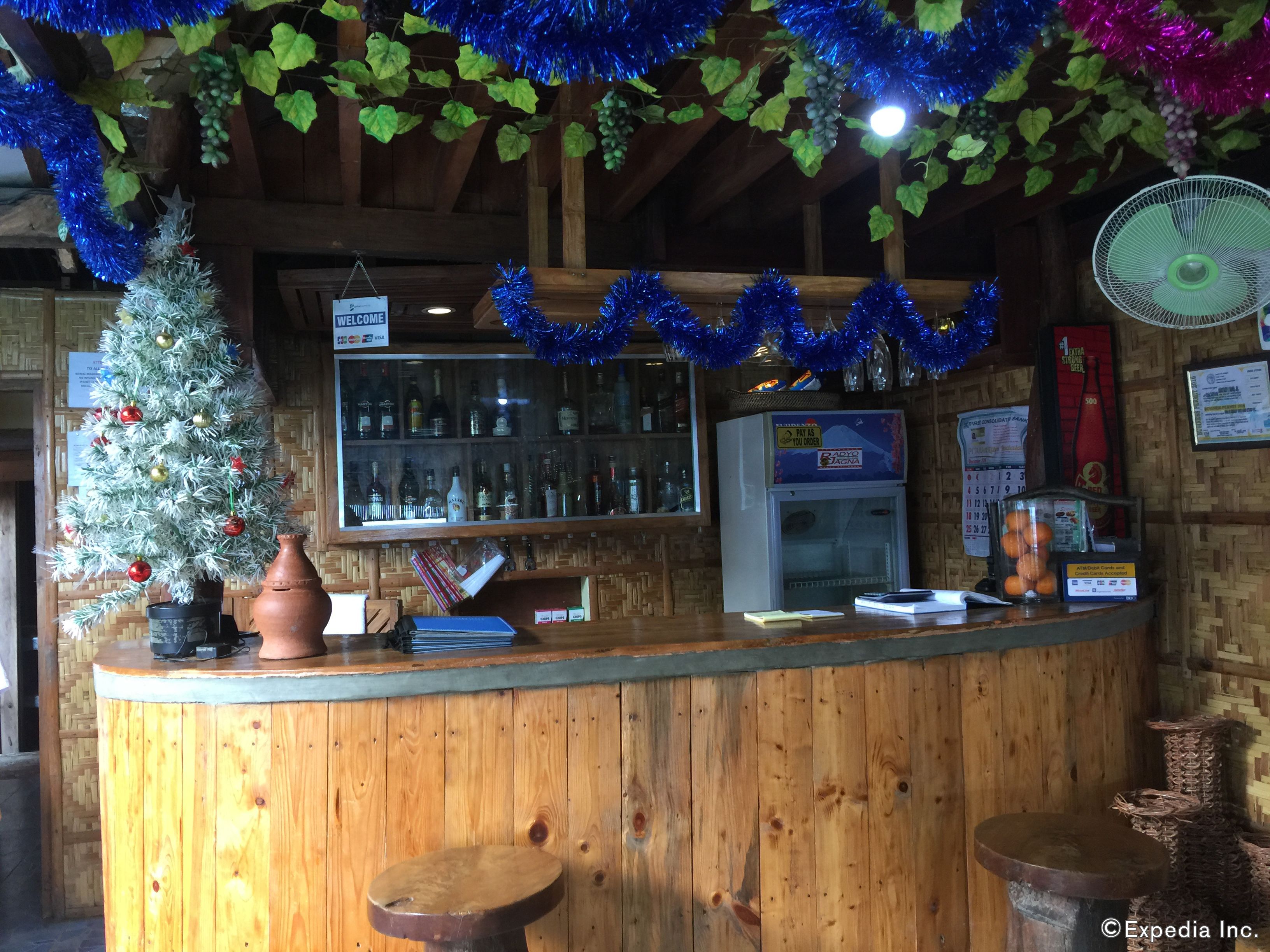 A rustic bar area with a wooden counter, a Christmas tree, and a refrigerator.