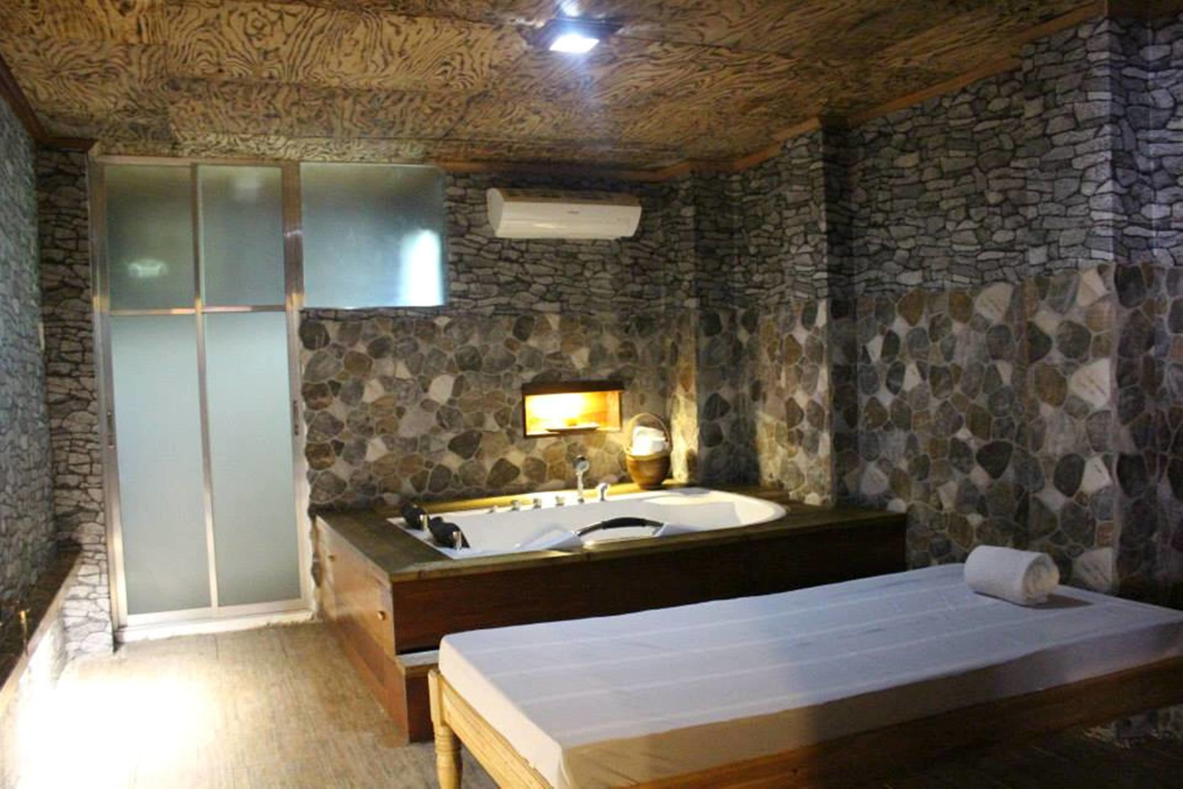 A bathroom with a stone wall, a wooden ceiling, a bathtub, a sink, and a toilet.