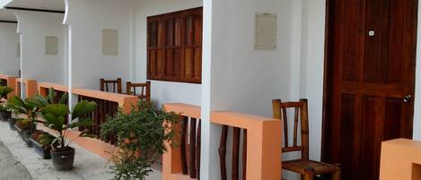 Un espacio al aire libre cubierto con plantas en macetas, sillas de madera y una alfombra roja que conduce a una puerta de madera.