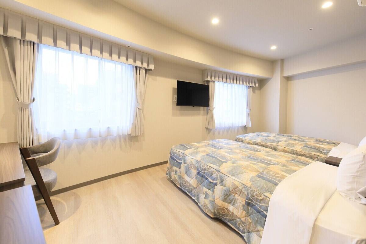 Habitación de hotel con dos camas, un televisor montado en la pared y un escritorio con una silla.