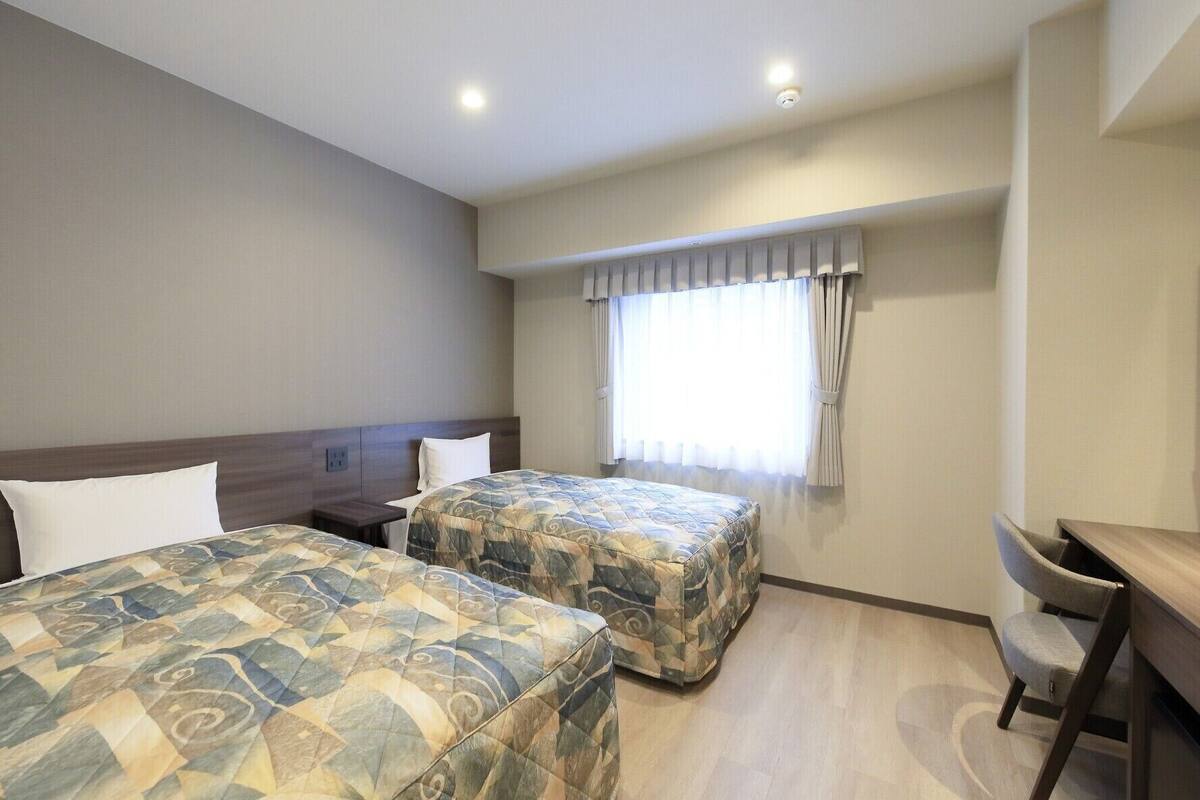 Habitación de hotel con dos camas, un escritorio y una ventana con cortinas.